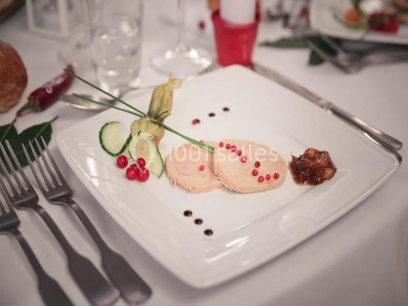 Assiette de foie gras décorée de groseilles, concombre, physalis et chutney, servie avec des touches de sauce balsamique.
