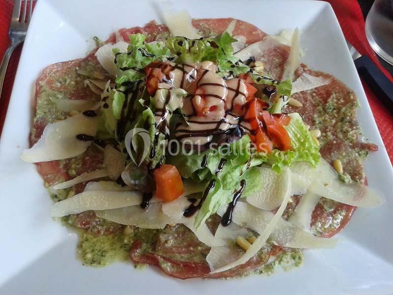 Assiette de carpaccio de bœuf garnie de salade, copeaux de parmesan, tomates et filet de sauce balsamique.