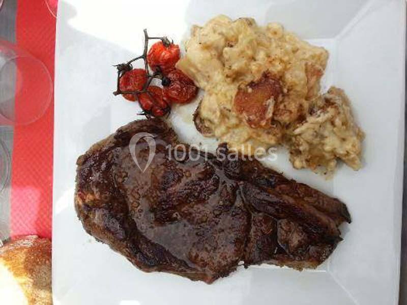 Assiette avec une pièce de viande grillée, gratin crémeux et tomates cerises rôties sur une table.