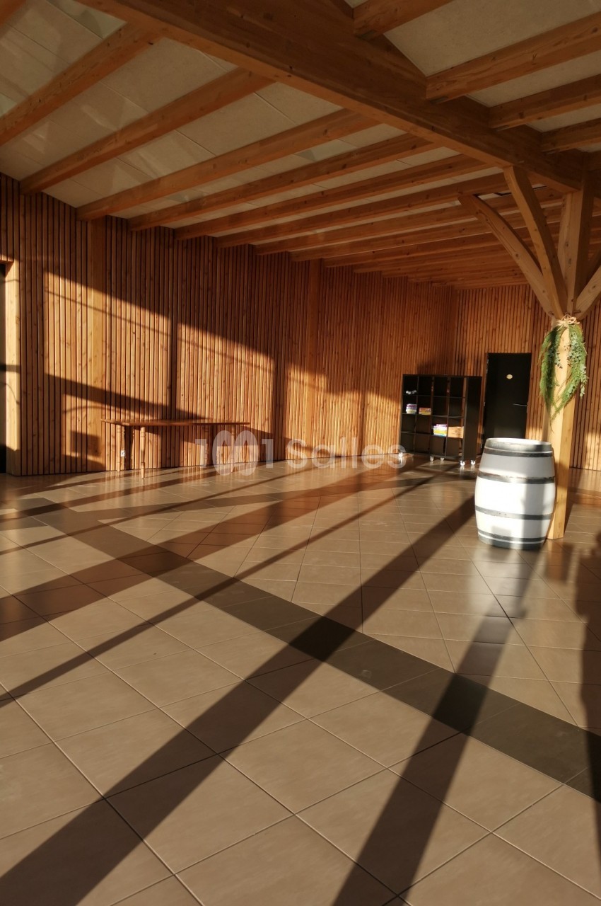 Salle lumineuse avec murs en bois, sol carrelé, tonneau blanc et ombres projetées par la lumière du soleil.