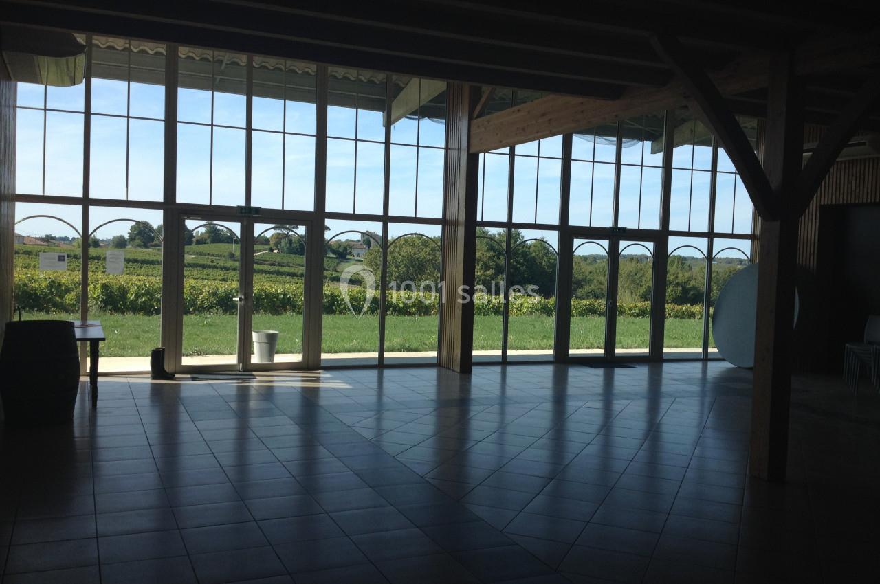 Salle lumineuse avec de grandes baies vitrées donnant sur un paysage de vignobles sous un ciel dégagé.
