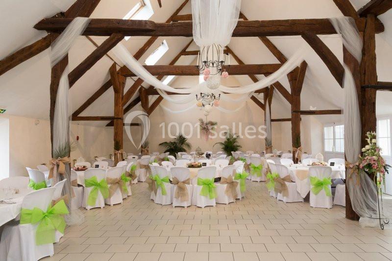 Salle de réception lumineuse avec poutres apparentes, tables décorées de nœuds verts et voilages suspendus.