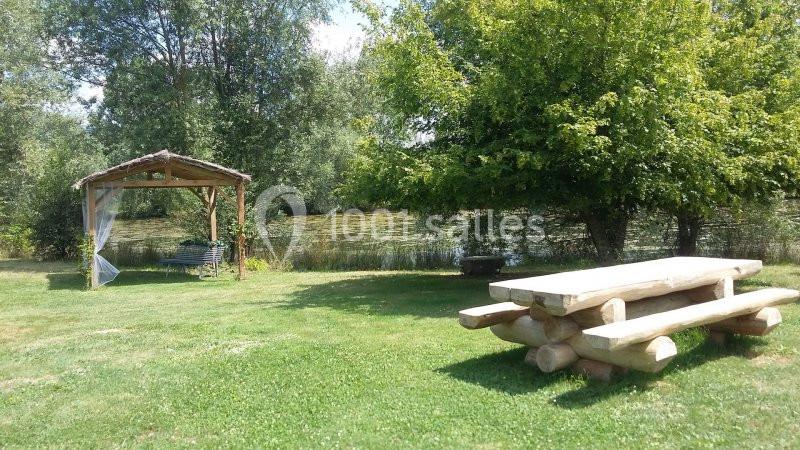 Table de pique-nique en bois et tonnelle près d'un étang entouré d'arbres dans un espace vert.