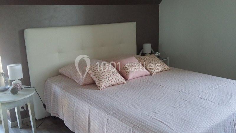 Lit double avec tête de lit blanche, drap rose pâle et coussins assortis dans une chambre lumineuse.