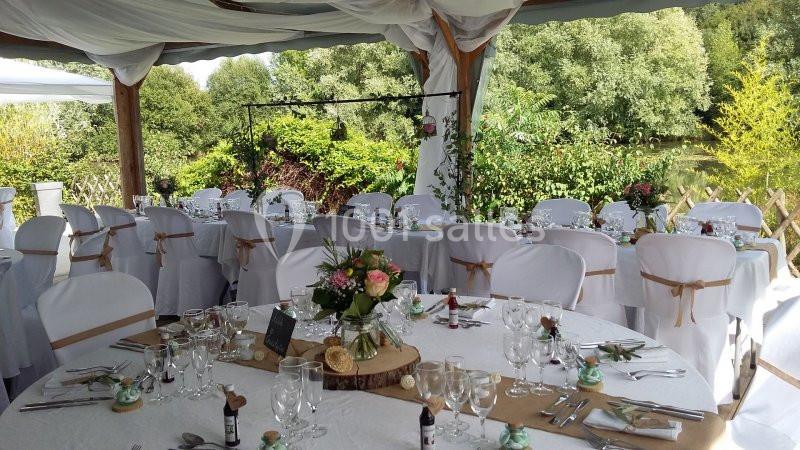 Salle de réception en extérieur décorée pour un mariage, avec tables rondes dressées et ornées de fleurs.