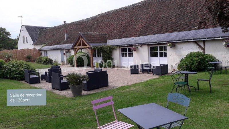 Espace extérieur avec mobilier de jardin devant une salle de réception à toit en tuiles, entourée de verdure.