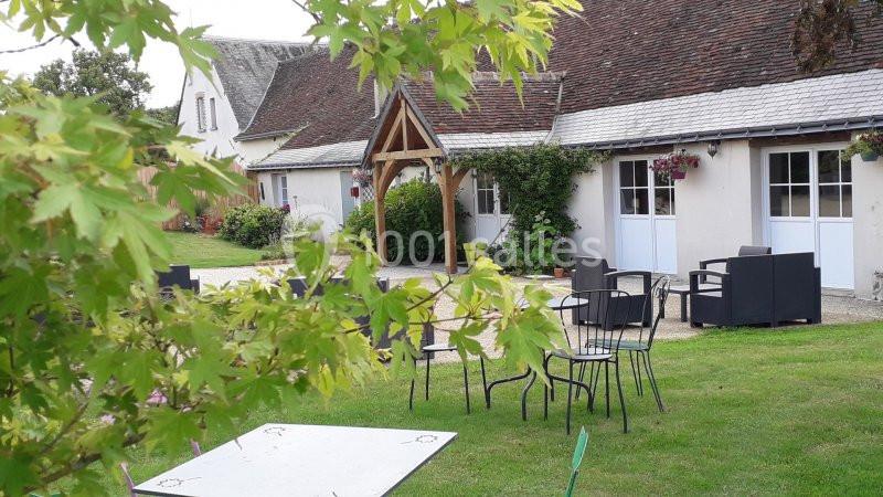 Espace extérieur avec pelouse, tables et chaises devant un bâtiment à toit en pente et porche en bois.