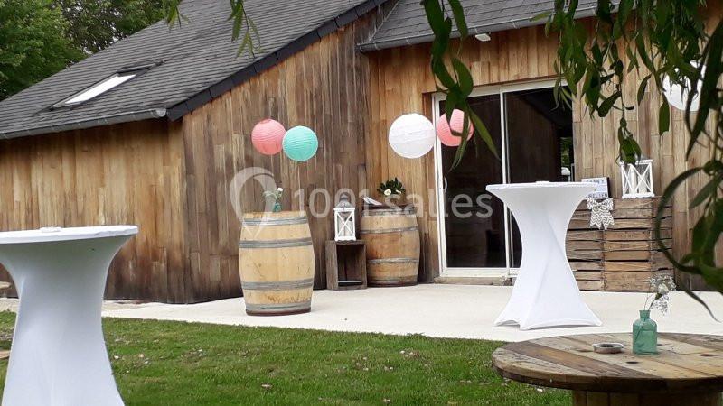 Terrasse d'une salle en bois décorée de lanternes et lampions colorés, avec tonneaux et tables hautes.