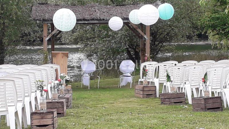 Chaises blanches alignées en extérieur face à une arche décorée de lanternes, près d'un plan d'eau.