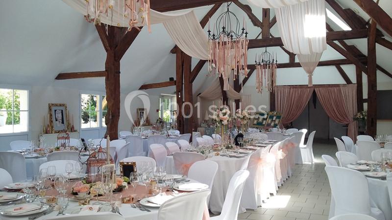 Salle de réception décorée pour un mariage, avec tables dressées, chaises blanches et éléments floraux élégants.
