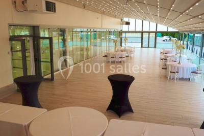 Salle de réception élégante avec tables décorées de nappes blanches, centres de table floraux et éclairage rose.