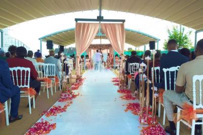 Salle de réception élégante avec tables décorées de nappes blanches, centres de table floraux et éclairage rose.