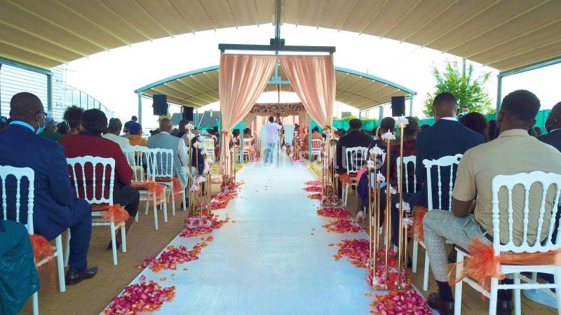 Allée centrale décorée de pétales de fleurs, entourée d'invités assis, lors d'une cérémonie en plein air sous une tente.