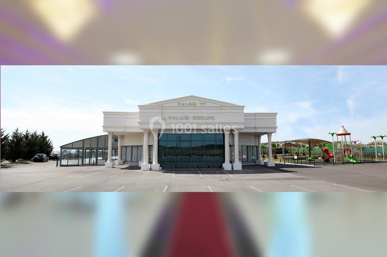 Façade d'un bâtiment blanc avec une architecture classique, entouré d'un parking et d'espaces verts.