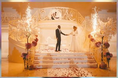 Salle de réception élégante avec tables décorées de nappes blanches, centres de table floraux et éclairage rose.
