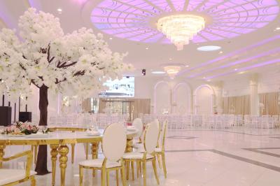 Salle de réception élégante avec tables décorées de nappes blanches, centres de table floraux et éclairage rose.