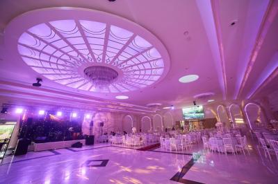 Salle de réception élégante avec tables décorées de nappes blanches, centres de table floraux et éclairage rose.