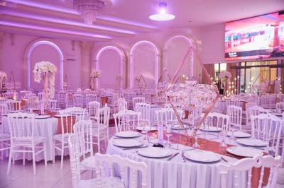 Salle de réception élégante avec tables décorées de nappes blanches, centres de table floraux et éclairage rose.