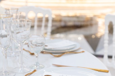 Salle de réception élégante avec tables décorées de nappes blanches, centres de table floraux et éclairage rose.