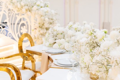 Salle de réception élégante avec tables décorées de nappes blanches, centres de table floraux et éclairage rose.