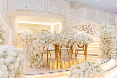Salle de réception élégante avec tables décorées de nappes blanches, centres de table floraux et éclairage rose.