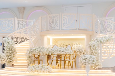Salle de réception élégante avec tables décorées de nappes blanches, centres de table floraux et éclairage rose.