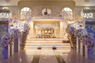 Salle de réception élégante avec tables décorées de nappes blanches, centres de table floraux et éclairage rose.