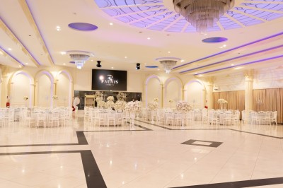 Salle de réception élégante avec tables décorées de nappes blanches, centres de table floraux et éclairage rose.