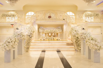 Salle de réception élégante avec tables décorées de nappes blanches, centres de table floraux et éclairage rose.