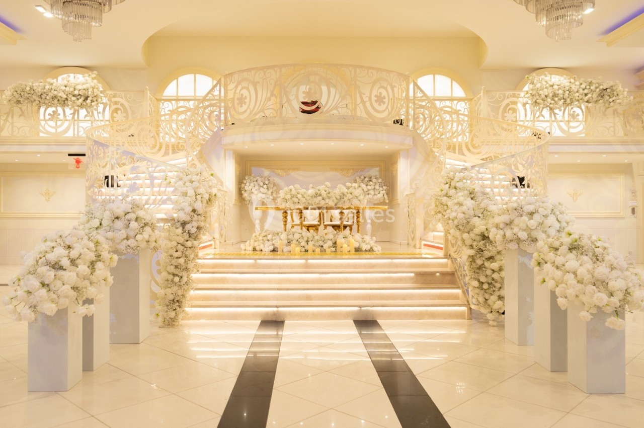 Escalier décoré de fleurs blanches menant à une scène ornée dans une salle lumineuse et élégante.