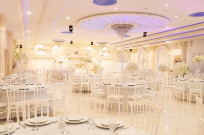 Salle de réception élégante avec tables décorées de nappes blanches, centres de table floraux et éclairage rose.