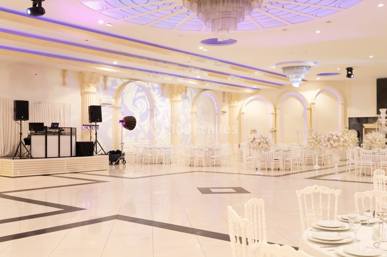 Salle de réception élégante avec tables dressées, chaises blanches et piste de danse, éclairée par des lumières tamisées.