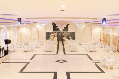 Salle de réception élégante avec tables décorées de nappes blanches, centres de table floraux et éclairage rose.