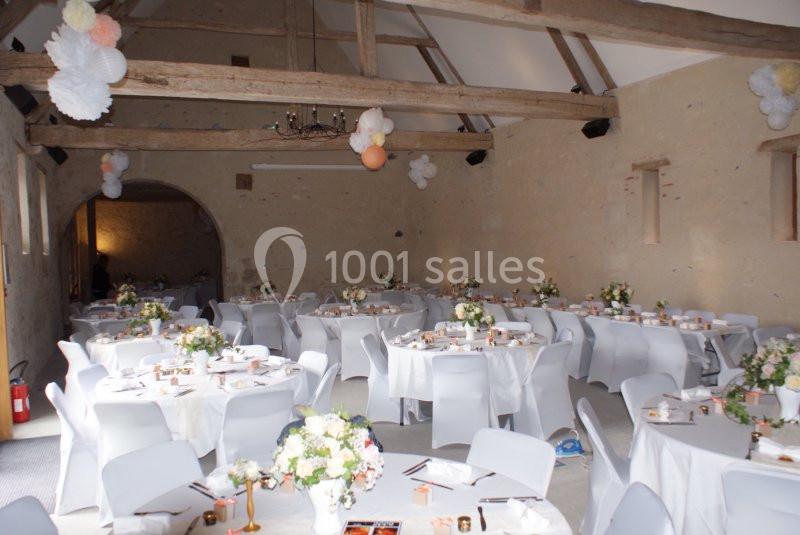Salle de réception avec tables rondes décorées de nappes blanches, fleurs et guirlandes suspendues au plafond.