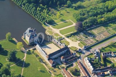 Salle en pierre avec poutres apparentes, tables rondes dressées et décorations lumineuses pour un événement.