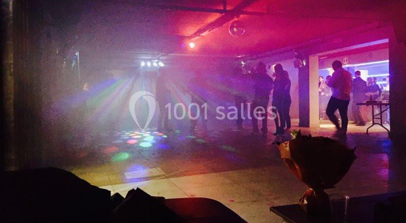 Des personnes dansent dans une salle sombre éclairée par des lumières colorées et un effet de fumée.