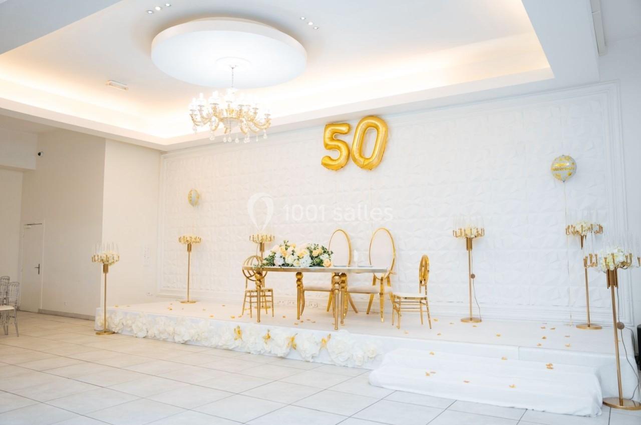 Location salle Viry-Châtillon (Essonne) - Glodie Evènements #3 Salle décorée pour un 50e anniversaire, avec ballons dorés, table ornée de fleurs et chaises élégantes sur une estrade.
