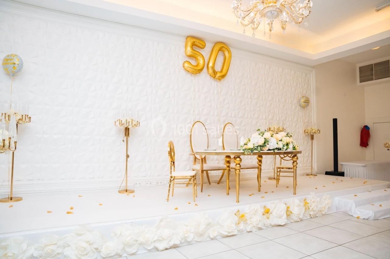 Location salle Viry-Châtillon (Essonne) - Glodie Evènements #5 Salle décorée pour une célébration avec une table ornée de fleurs blanches et des ballons dorés formant le chiffre 50.