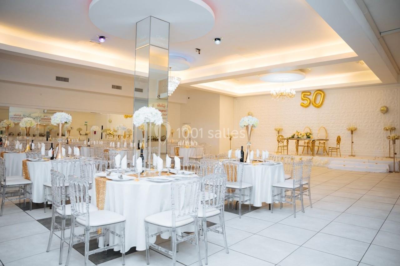 Location salle Viry-Châtillon (Essonne) - Glodie Evènements #8 Salle de réception élégante décorée en blanc et or, avec tables dressées et ballon ’50’ en arrière-plan.