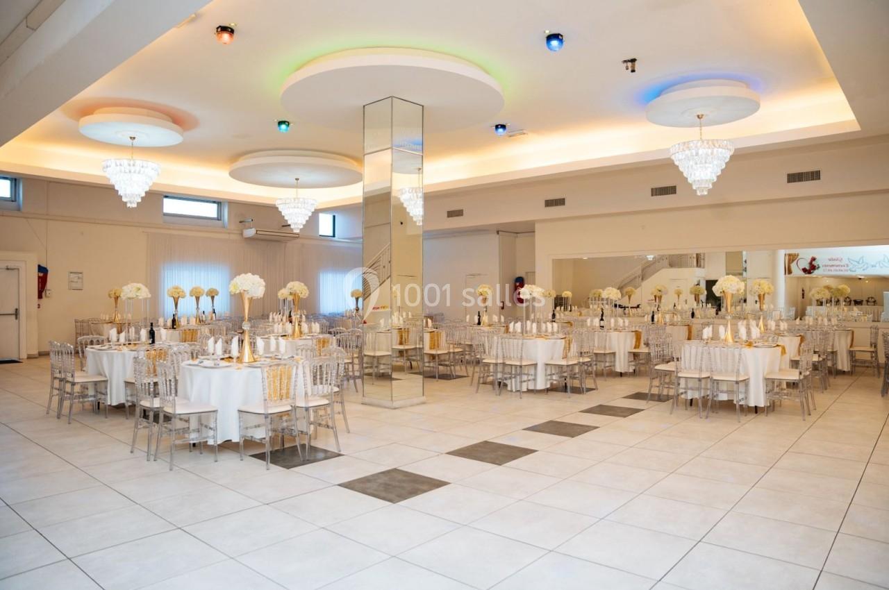 Location salle Viry-Châtillon (Essonne) - Glodie Evènements #13 Salle de réception lumineuse avec tables décorées de fleurs blanches, chaises transparentes et lustres suspendus.