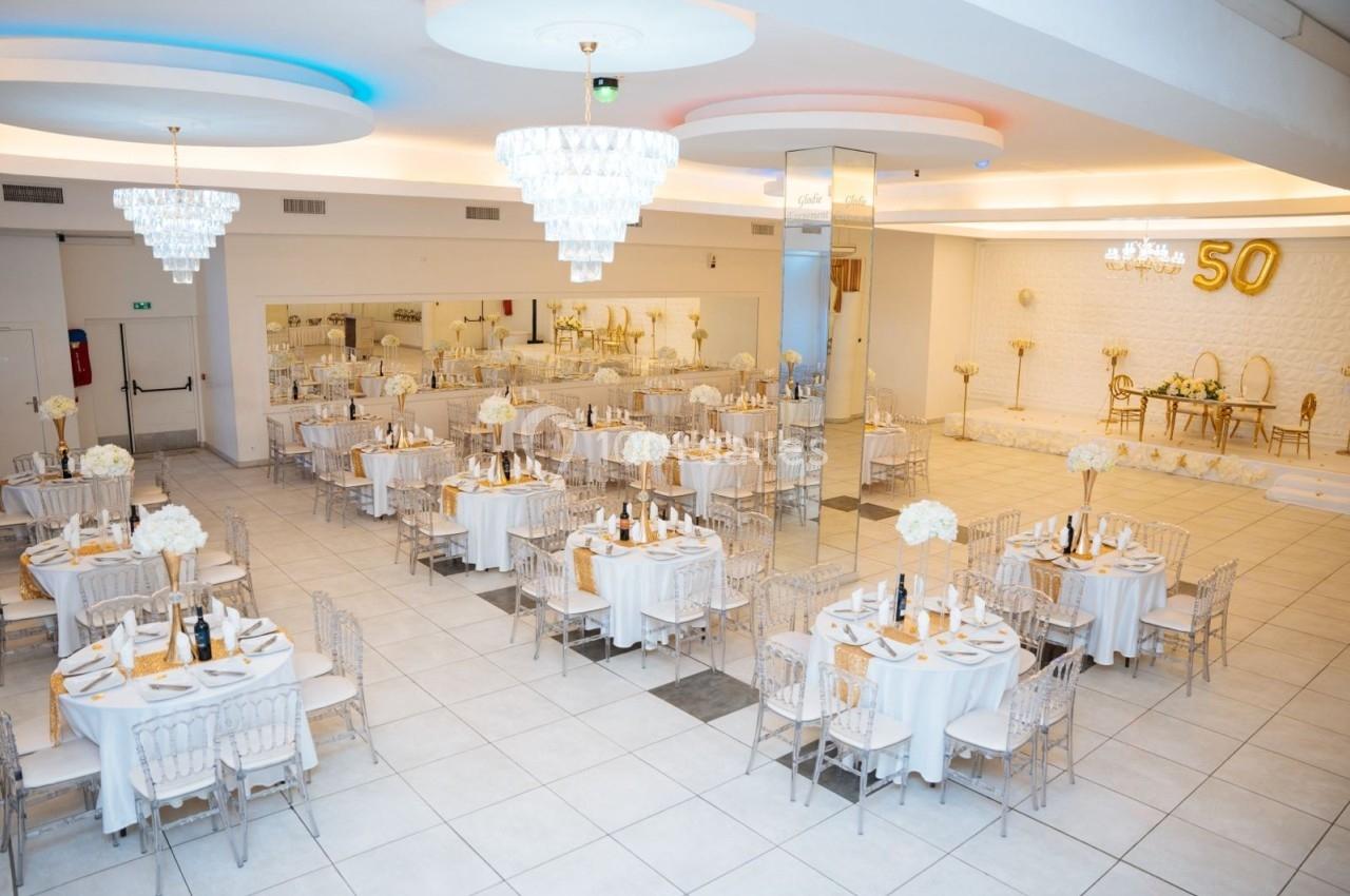 Location salle Viry-Châtillon (Essonne) - Glodie Evènements #15 Salle de réception élégante avec tables rondes dressées, décorations blanches et dorées, et un chiffre 50 en ballon.
