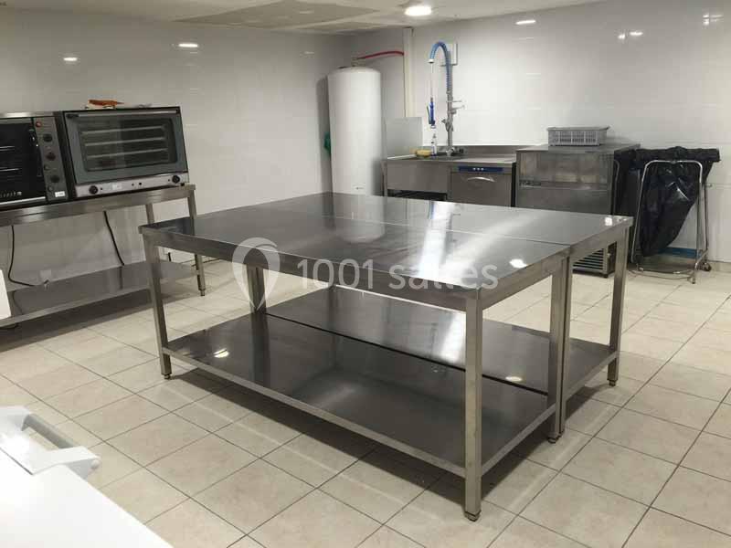 Table en inox avec étagère inférieure dans une cuisine professionnelle équipée de fours et d'équipements.