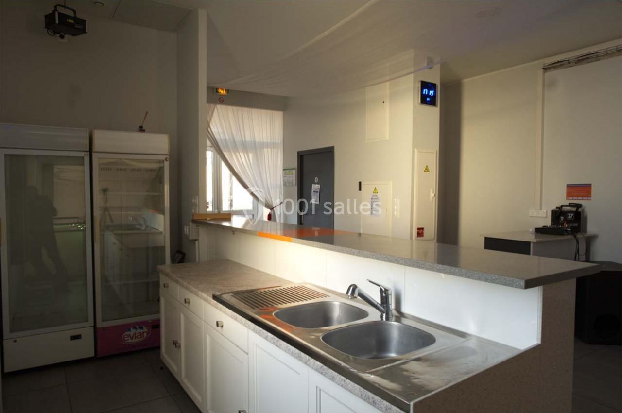 Cuisine lumineuse avec un évier double, un comptoir, un réfrigérateur vitré et une machine à café en arrière-plan.