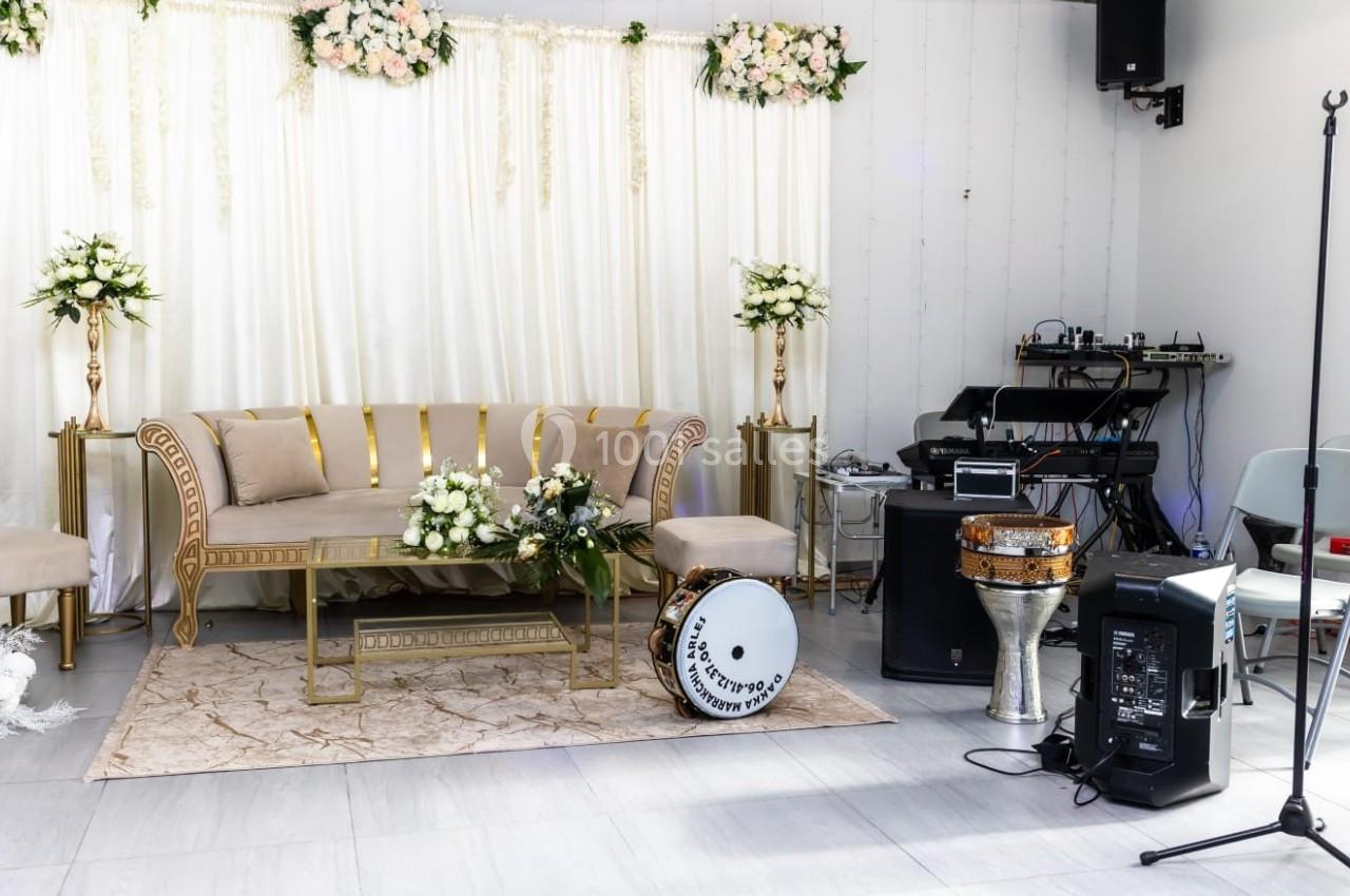 Salon décoré pour un événement avec canapé doré, fleurs blanches, instruments de musique et équipement audio.