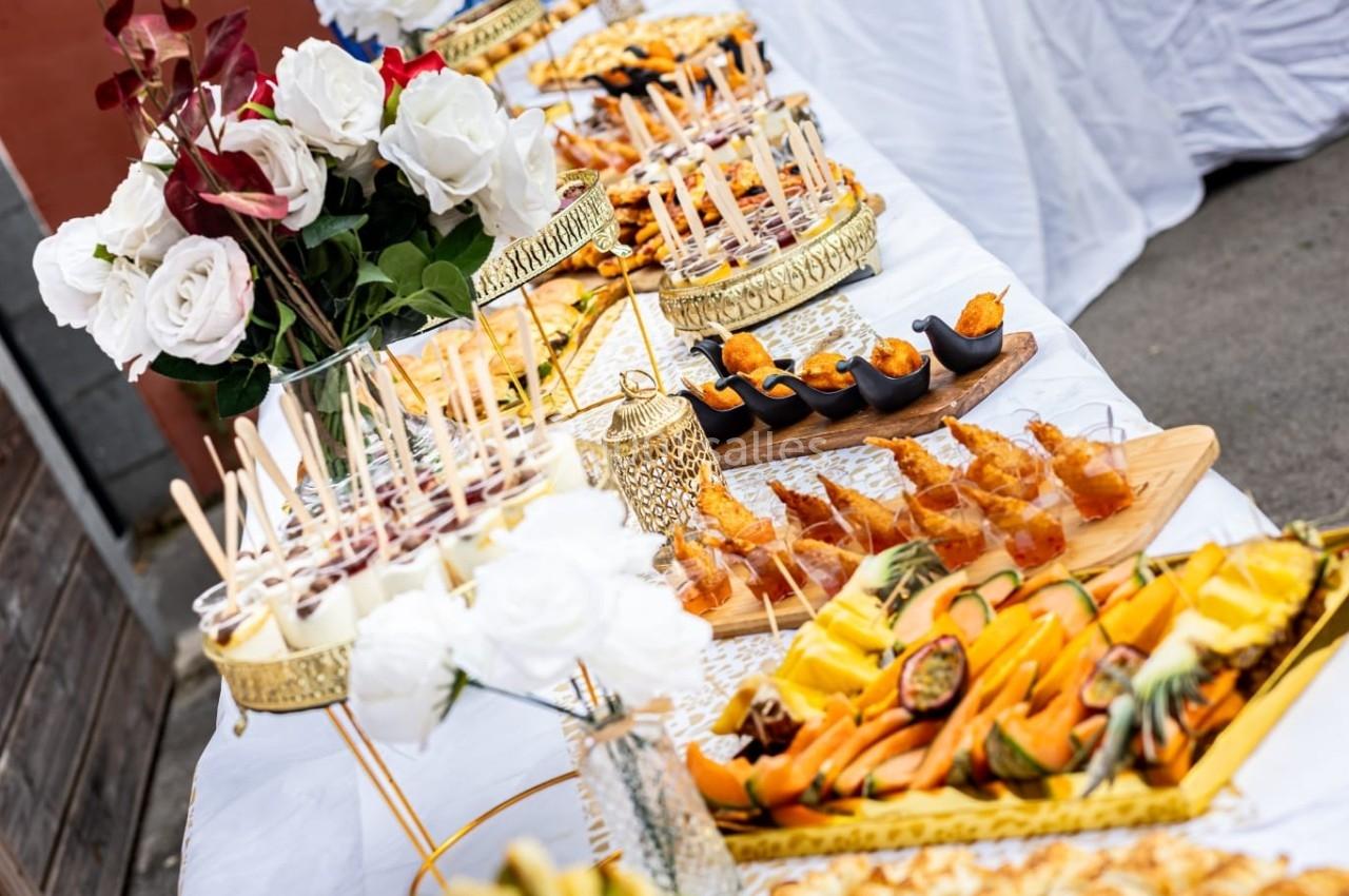 Buffet élégant avec assortiments de brochettes, fruits frais, verrines et fleurs décoratives sur une table blanche.