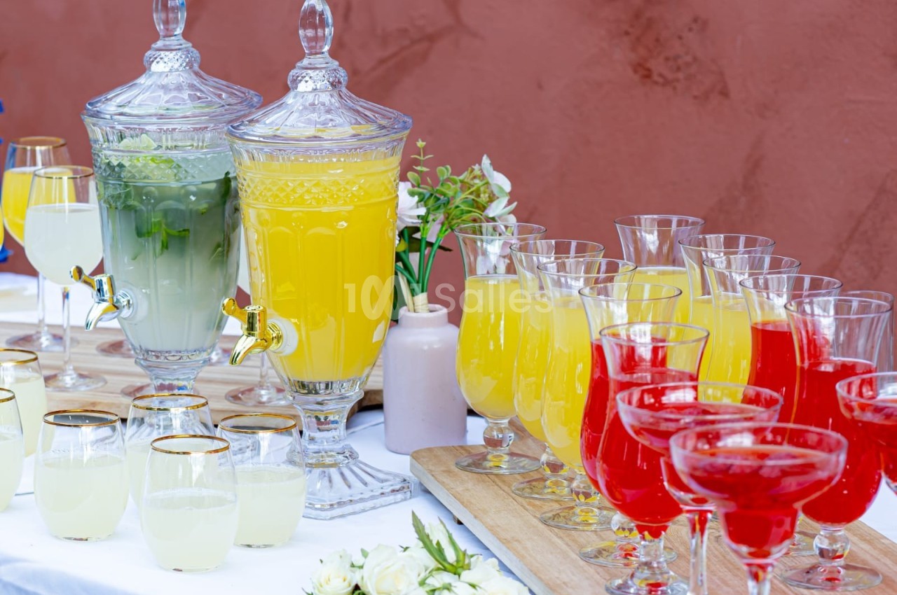 Deux distributeurs de boissons et des verres remplis de jus colorés disposés sur une table blanche.