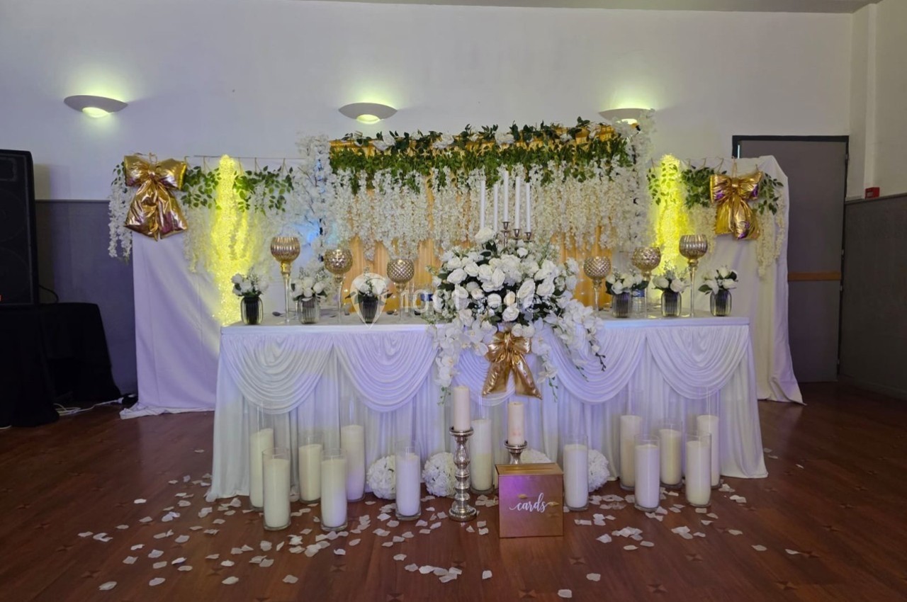 Table décorée pour un mariage avec fleurs blanches, chandeliers, guirlandes lumineuses et bougies sur un sol en bois.