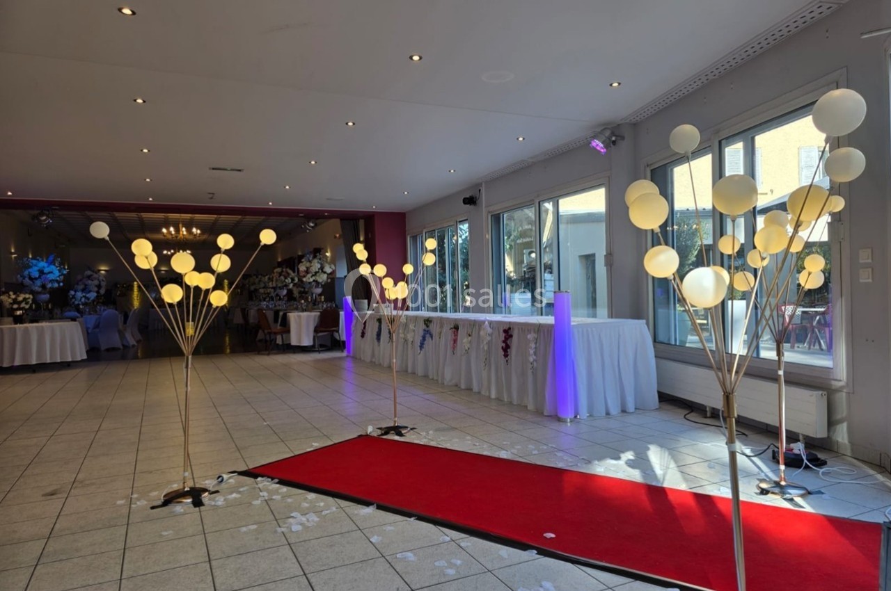 Salle de réception décorée avec un tapis rouge, des ballons lumineux et des tables dressées en arrière-plan.