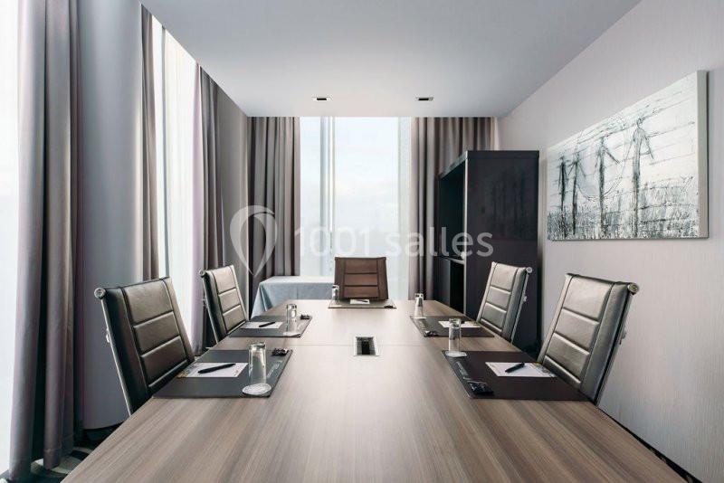 Location salle Mons (Hainaut) - Congrès Hôtel Mons Van Der Valk #3 Salle de réunion moderne avec table en bois, chaises en cuir noir, blocs-notes, stylos et grandes fenêtres.