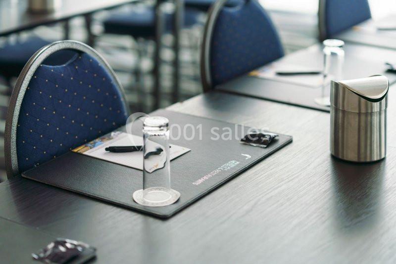 Location salle Mons (Hainaut) - Congrès Hôtel Mons Van Der Valk #9 Salle de réunion avec des chaises bleues, des tables noires, des sous-mains, des stylos et des verres disposés.